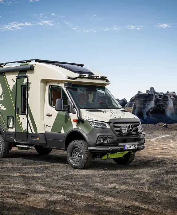 Offroad-Wohnmobil Mercedes Sprinter mit Camouflage-Design in einer steinigen Wüstenlandschaft unter blauem Himmel.